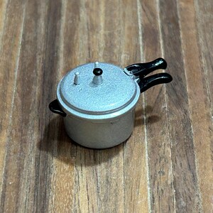 Peut inclure: Une cocotte-minute en argent avec une poignée noire et un couvercle en argent. La cocotte-minute a un petit bouton sur le couvercle.