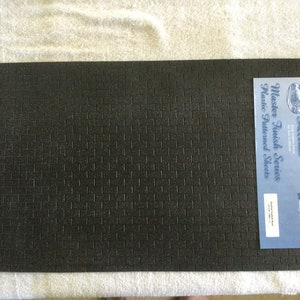 May include: A sheet of black textured plastic for model building. The sheet has a brick pattern and is labelled "Miniature Accents Master Finish Series Plastic Patterned Sheets".