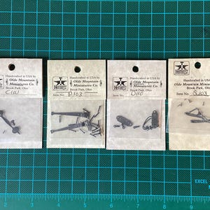 May include: Four small packages containing miniature metal hardware pieces. Each package has a label with the text "Handcrafted in USA by Olde Mountain Miniatures Co. Brook Park, Ohio" and an item number: "C10", "P103", "D110", and "S103".