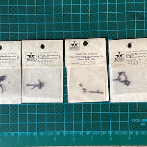 May include: Four white cards with black text and images of small metal parts. The cards are labelled with item numbers: CI10, CI11, CI20, and CI25. The text on the cards reads "Handcrafted in USA by Olde Mountain Miniatures Co. Brook Park, Ohio".