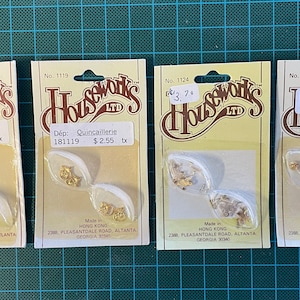 May include: Four packs of gold-coloured metal hardware, each with a white background and a yellow label. The labels include the text "Houseworks LTD" and the product number, description, and price. The packs are on a green grid background.