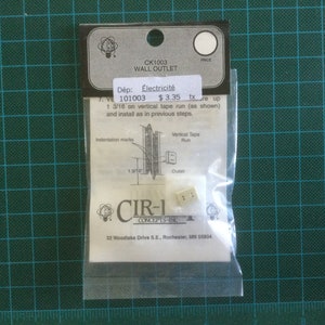 May include: A packaged wall outlet, labelled "CK1003 WALL OUTLET," with the text "Électricité" and "1 3/16" measurements (approximately 3 cm). The package includes a small, beige outlet and a diagram. The brand is CIR-1 CONCEPTS INC.