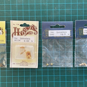 May include: Four packets of miniature hardware for dollhouses. The packets are labelled with the name "Houseworks LTD" and the price in US dollars. The packets contain various items, including screws, hinges, and a key.