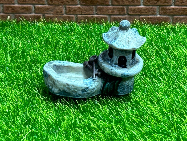 May include: A small, gray stone fountain with a pagoda-style roof. The fountain is designed for a miniature garden or fairy garden.