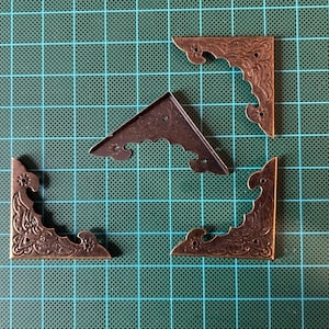 Antique brass-finished metal corners. Nails included. Pack of 4. For craft projects.
