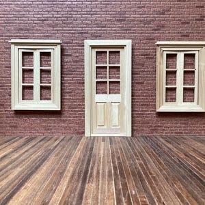 May include: A miniature wooden door and two windows are set against a brick wall. The door is centered, flanked by windows. The floor is made of wooden planks. The windows and door have a light wood finish.