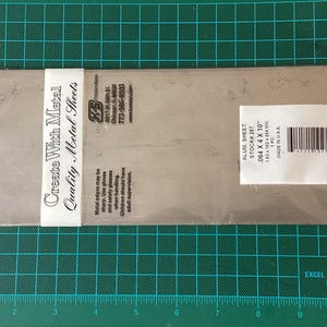 Peut inclure: Une feuille de métal en aluminium, d'une épaisseur de 1,63 mm, d'une largeur de 102 mm et d'une longueur de 254 mm. La feuille est emballée dans un sac en plastique transparent avec une étiquette indiquant "Create With Metal Quality Metal Sheets" et comprenant le nom de l'entreprise, l'adresse et le numéro de téléphone. L'étiquette comprend également un avertissement concernant les bords tranchants et la nécessité d'une supervision d'un adulte.