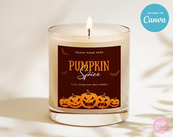 May include: A lit pumpkin spice soy wax candle in a clear glass jar. The label is dark brown with orange text and jack-o'-lantern graphics. The candle is 11 oz.