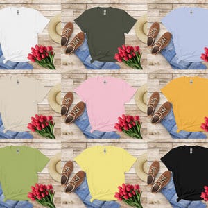 K&ouml;nnte beinhalten: Neun verschiedenfarbige T-Shirts, darunter Wei&szlig;, Olivgr&uuml;n und Schwarz, werden mit Jeans, Schuhen, H&uuml;ten und Str&auml;u&szlig;en roter Tulpen pr&auml;sentiert. Die Hemden sind auf einer hellen Holzmaserung angeordnet.
