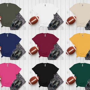 K&ouml;nnte beinhalten: Neun verschiedenfarbige T-Shirts, jeweils kombiniert mit einem Football und Turnschuhen. Farben sind Olivgr&uuml;n, Wei&szlig;, Beige, Marineblau, Burgunderrot, Gelb, Pink, Schwarz und Dunkelgr&uuml;n. Die Shirts sind auf hellem Holzmaserungshintergrund angeordnet.