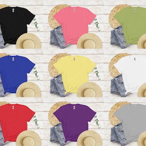K&ouml;nnte beinhalten: Neun farbenfrohe T-Shirts in Schwarz, Rosa, Gr&uuml;n, Blau, Gelb, Wei&szlig;, Rot, Lila und Grau werden gezeigt. Jedes Shirt ist mit Jeans und einem Strohhut kombiniert, was eine l&auml;ssige, sommerliche &Auml;sthetik erzeugt. Die Shirts sind auf einem hellen Holzmaserungshintergrund angeordnet.
