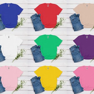 K&ouml;nnte beinhalten: Neun farbige T-Shirts in Blau, Rot, Beige, Wei&szlig;, Gr&uuml;n, Lila, Rosa, Gelb und Pink, kombiniert mit blauen Jeans. Jedes Set ist auf einer wei&szlig;en Holzoberfl&auml;che mit einem Zweig Gr&uuml;n angeordnet.