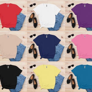 K&ouml;nnte beinhalten: Neun farbige T-Shirts in Rot, Wei&szlig;, Lila, Beige, Marineblau, Pink, Schwarz, Gelb und T&uuml;rkis. Jedes Shirt ist mit blauen Jeans, schwarzen Loafern und Sonnenbrillen kombiniert. Die Shirts sind auf einer hellen Holzmaserung angeordnet.
