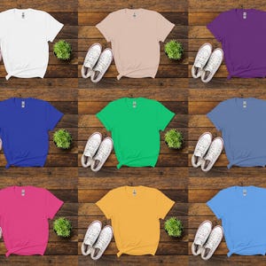 K&ouml;nnte beinhalten: Neun einfarbige T-Shirts in Wei&szlig;, Beige, Lila, Blau, Gr&uuml;n, Hellblau, Pink, Gelb und Hellblau. Jedes Shirt wird mit wei&szlig;en Turnschuhen und einer kleinen gr&uuml;nen Pflanze auf einem Holzgrund gezeigt.