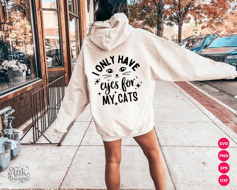 以下が含まれることがあります： 「I ONLY HAVE eyes for MY CATS」の黒い文字が入ったクリーム色のフード付きスウェットシャツ。猫の目と星のデザイン。スウェットシャツは屋外で着用されています。