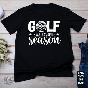 May include: Black t-shirt with the text "GOLF is my favorite season" in white. The word "GOLF" is above a golf ball graphic. The text is centered on the shirt. The shirt is on a light wood surface.
