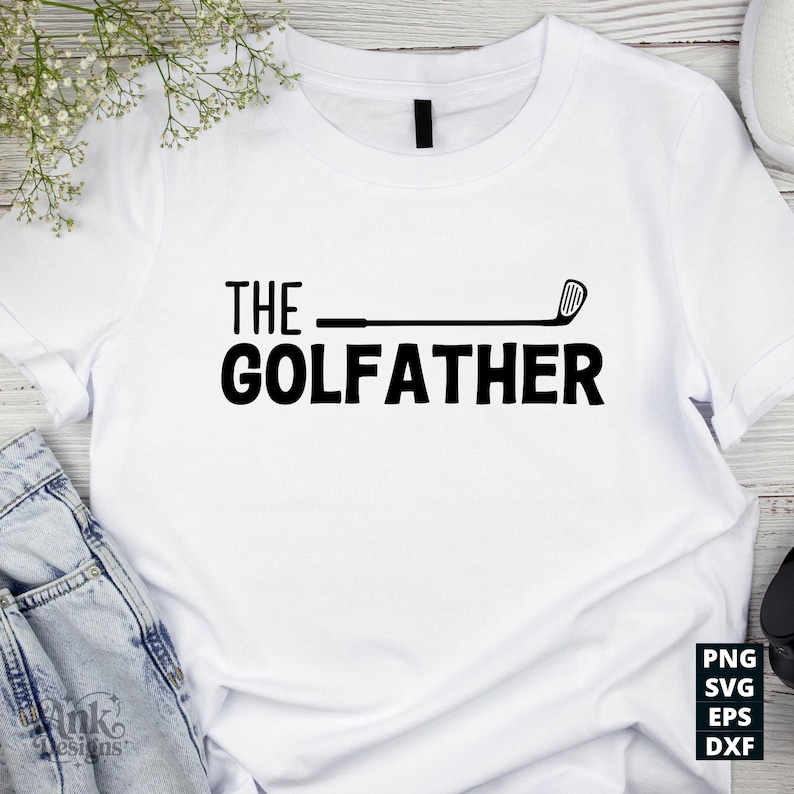 May include: White t-shirt with the text "THE GOLFFATHER" in bold black letters. A golf club graphic replaces the "F" in "GOLFFATHER". The shirt is a casual style, suitable for golf enthusiasts.