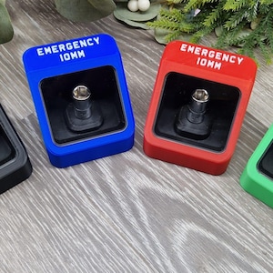 May include: Four brightly coloured emergency 10mm socket holders. The holders are black, blue, red, and green. Each holder has a rectangular shape with the text "EMERGENCY 10MM" in white. A silver socket is visible inside each holder.