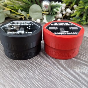 May include: Two small, round containers with breakable glass tops. The containers are labeled "IN CASE OF EMERGENCY" and "10MM BREAK GLASS". One container is black and the other is red.