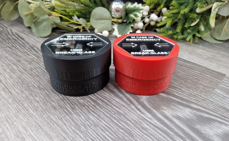 May include: Two small, round containers with breakable glass tops. The containers are labeled "IN CASE OF EMERGENCY" and "10MM BREAK GLASS". One container is black and the other is red.