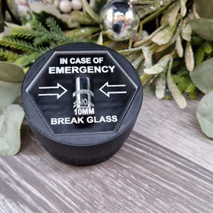May include: A black hexagonal box with a clear top that says "IN CASE OF EMERGENCY" and "BREAK GLASS". A silver 10mm socket is visible inside the box.