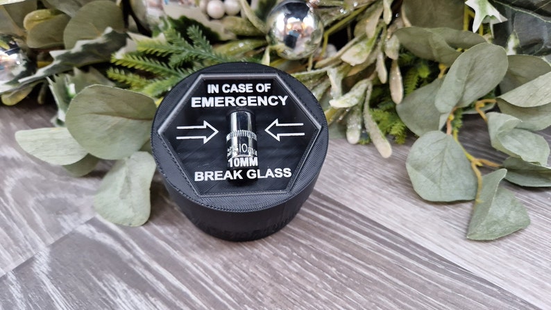 May include: A black hexagonal box with a clear top that says "IN CASE OF EMERGENCY" and "BREAK GLASS". A silver 10mm socket is visible inside the box.