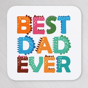 以下が含まれることがあります： 恐竜のようなデザインのカラフルなスタイリッシュな文字で「BEST DAD EVER」と書かれた白いコースターです。