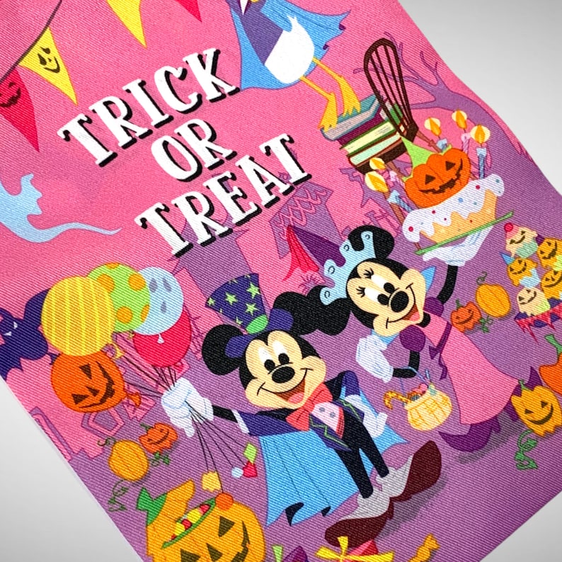 Puede incluir: Una bolsa de tela rosa y morada con tem&aacute;tica de Halloween con el texto "Trick or Treat" e im&aacute;genes de Mickey Mouse y Minnie Mouse vestidos con disfraces. La bolsa tambi&eacute;n presenta una variedad de im&aacute;genes con tem&aacute;tica de Halloween, como calabazas, ma&iacute;z dulce y fantasmas.