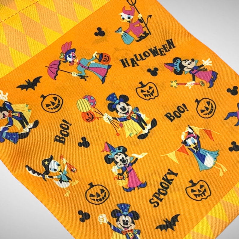 Puede incluir: Tela naranja con tem&aacute;tica de Halloween con Mickey Mouse y otros personajes de Disney. La tela tiene un patr&oacute;n repetitivo de calabazas, fantasmas, murci&eacute;lagos y las palabras "Boo!" y "Spooky".
