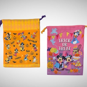 Puede incluir: Dos bolsas de truco o trato con tem&aacute;tica de Halloween. La bolsa de la izquierda es naranja con un patr&oacute;n de diamantes y presenta a Mickey Mouse y sus amigos. La bolsa de la derecha es rosa con un patr&oacute;n morado y blanco y presenta a Mickey Mouse y Donald Duck. Ambas bolsas tienen el texto "Trick or Treat" y "Boo!" impreso.