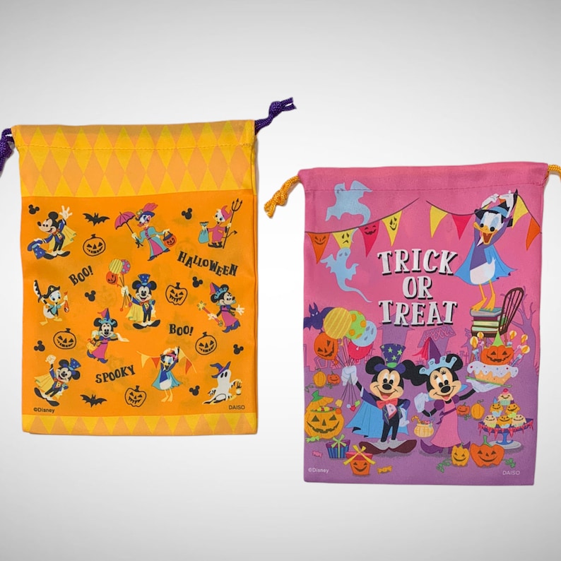 Puede incluir: Dos bolsas de truco o trato con tem&aacute;tica de Halloween. La bolsa de la izquierda es naranja con un patr&oacute;n de diamantes y presenta a Mickey Mouse y sus amigos. La bolsa de la derecha es rosa con un patr&oacute;n morado y blanco y presenta a Mickey Mouse y Donald Duck. Ambas bolsas tienen el texto "Trick or Treat" y "Boo!" impreso.
