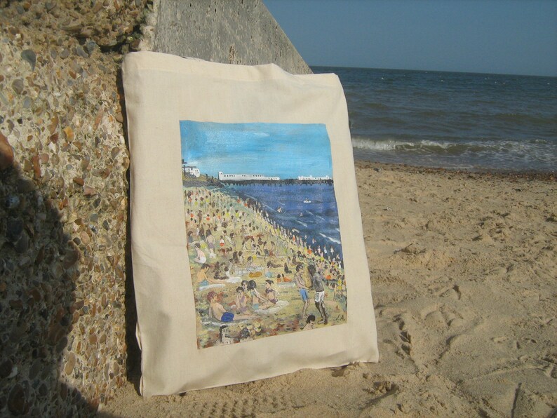 Może przedstawiać: Biała torba z pł&oacute;tna z kolorowym obrazem przedstawiającym scenę plażową. Obraz przedstawia pomost, błękitny ocean i wiele os&oacute;b na plaży.