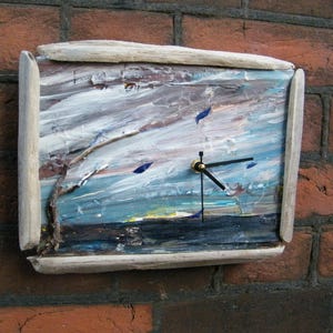 May include: A rectangular wall clock with a painted landscape scene. The clock face features a sky with blue, white, and gray brushstrokes, and a dark blue and black base. The clock is framed with light-colored wood.