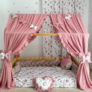 May include: A pink canopy bed with a wooden frame, draped with matching curtains and butterfly decorations. The bed has a floral patterned mattress and a heart-shaped pillow, creating a cosy and whimsical atmosphere.