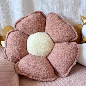 K&ouml;nnte beinhalten: Ein pl&uuml;schiges, blumenf&ouml;rmiges Kissen in Rosa mit einem wei&szlig;en Zentrum. Das Kissen ist aus weichem, flauschigem Stoff und hat eine leicht strukturierte Oberfl&auml;che.