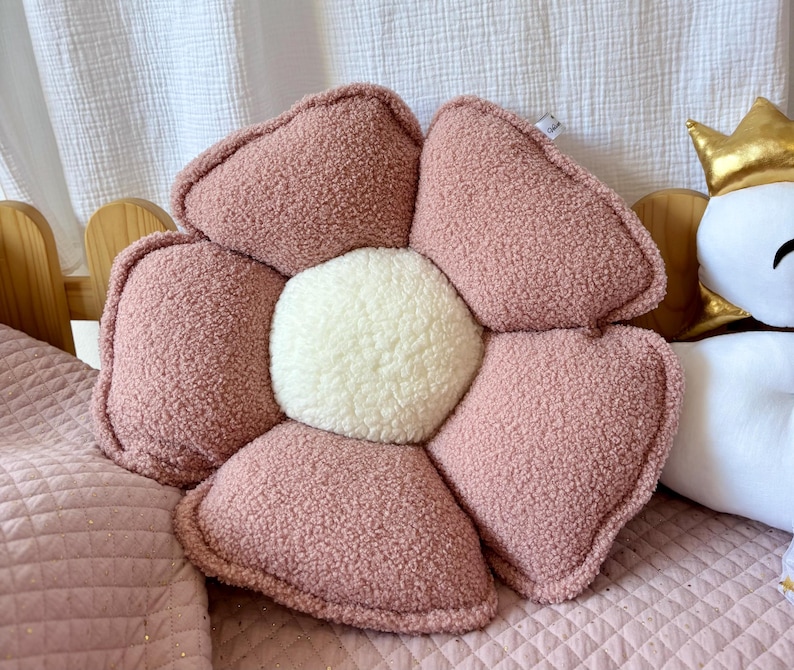 K&ouml;nnte beinhalten: Ein pl&uuml;schiges, blumenf&ouml;rmiges Kissen in Rosa mit einem wei&szlig;en Zentrum. Das Kissen ist aus weichem, flauschigem Stoff und hat eine leicht strukturierte Oberfl&auml;che.