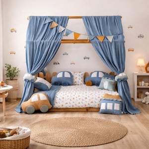 Könnte beinhalten: Ein Kinderbett mit Holzrahmen, drapiert mit blauen Vorhängen und mit Kissen und Bettwäsche im Autodesign dekoriert. Der Raum verfügt über einen runden Jute-Teppich und Autoaufkleber an der Wand, was eine spielerische und gemütliche Atmosphäre schafft.