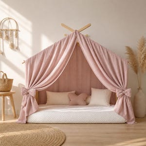 May include: A pink canopy bed with a wooden frame and draped fabric. The bed features a white quilted mattress and decorative pillows. The canopy is tied with large bows. A round woven rug is in the foreground.