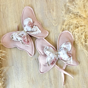 May include: Two pink butterfly decorations. The wings are a solid pink, and the centre has a floral pattern in white, pink, and green. The butterflies are made of soft fabric, suitable for a nursery.