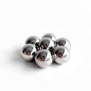 May include: A group of eight silver metal balls arranged in a circular pattern on a white surface.
