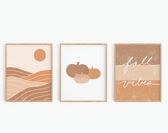 May include: Three minimalist fall-themed prints with a brown, orange, and white color scheme. The first print features a landscape with rolling hills and a sun. The second print features three pumpkins. The third print features the text "fall vibes" in white script.