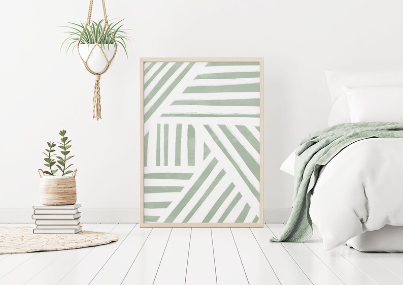 K&ouml;nnte beinhalten: Ein gerahmter abstrakter Druck mit einem geometrischen Muster aus wei&szlig;en Linien auf einem Salbeigr&uuml;n-Hintergrund. Der Druck h&auml;ngt an einer wei&szlig;en Wand &uuml;ber einem Bett mit wei&szlig;en Bettw&auml;sche und einer Salbeigr&uuml;n-Decke.