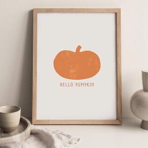 Może przedstawiać: Wydruk w ramie z prostym pomarańczowym sylwetem dyni i tekstem "HELLO PUMPKIN" w kolorze białym.