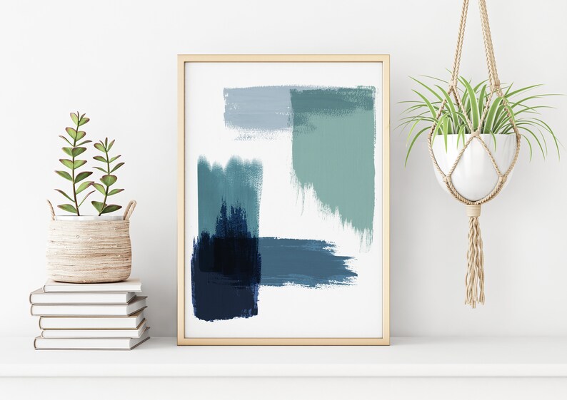 May include: Abstract art print with blue and green brushstrokes in a wooden frame. The print is hanging on a white wall with a potted plant on a shelf below.