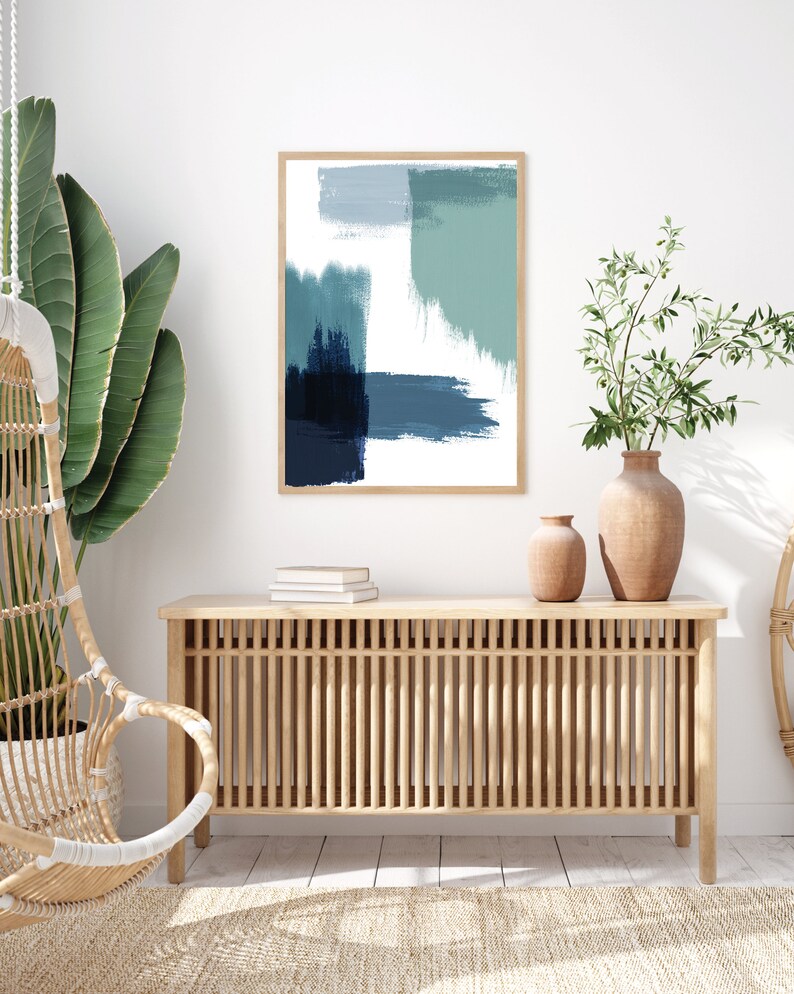 May include: A wooden console table with a slatted design and a framed abstract painting with blue and green brushstrokes hanging above it. Two potted plants are on the floor next to the table.