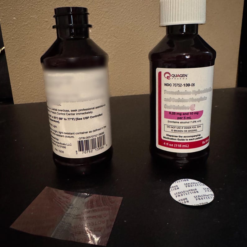 K&ouml;nnte beinhalten: Zwei dunkelbraune Medizinflaschen mit wei&szlig;en Etiketten und schwarzen Verschl&uuml;ssen werden gezeigt. Eine Flasche hat ein wei&szlig;es Etikett mit Text, die andere ein rosa-wei&szlig;es Etikett mit dem Markennamen "QUAGEN" und Produktinformationen. Ein kleines, klares, versiegeltes Folienpaket und ein wei&szlig;er "SEALED FOR YOUR PROTECTION"-Siegel sind ebenfalls vorhanden.