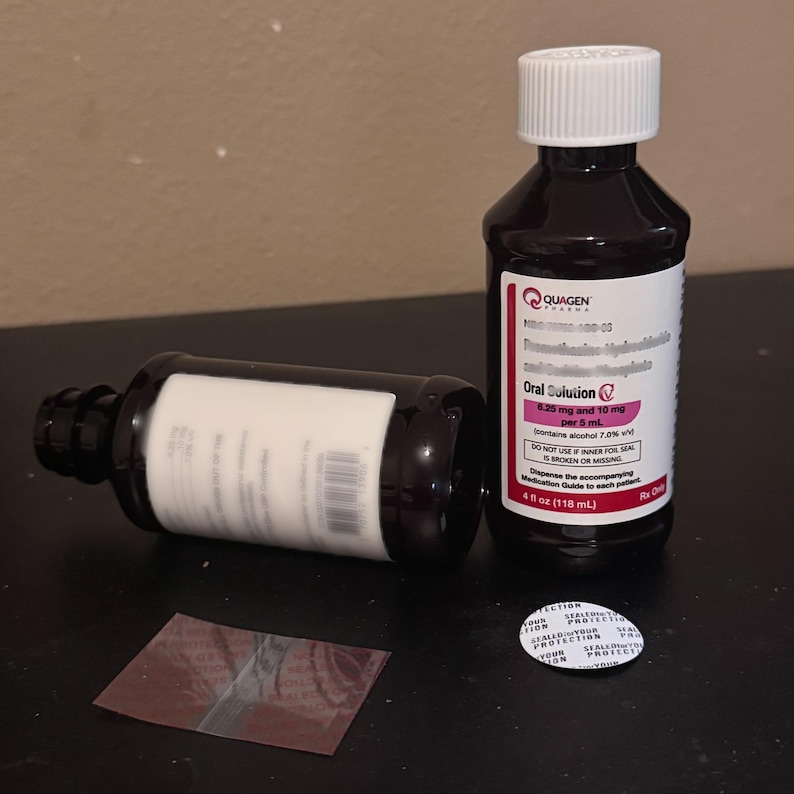 K&ouml;nnte beinhalten: Zwei dunkelbraune Medizinflaschen mit wei&szlig;en Etiketten und Verschl&uuml;ssen. Eine Flasche steht aufrecht, die andere liegt auf der Seite. Auf den Etiketten steht "Oral Solution" und enthalten Dosierungsinformationen. Ein Foliensiegel und ein Flaschensiegel sind ebenfalls vorhanden.