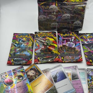 May include: A display box of Pokemon Trading Card Game booster packs labeled Pitch Black, alongside several individual booster packs and a collection of loose trading cards featuring various characters, including a Mega Slowbro EX card.