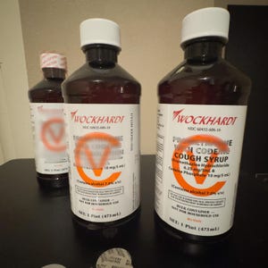 May include: Three brown bottles of Wockhardt cough syrup with white labels and caps. The labels display the text "Promethazine Codeine Solution" and "Cough Syrup". Each bottle contains 1 pint (473 mL).