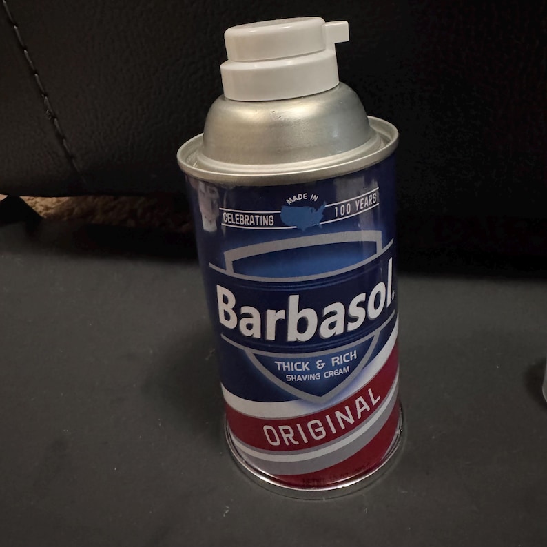 May include: A can of Barbasol shaving cream. The can is blue with white and red accents, and features the brand name and the words "Thick & Rich Shaving Cream" and "Original". The top is silver with a white dispenser.
